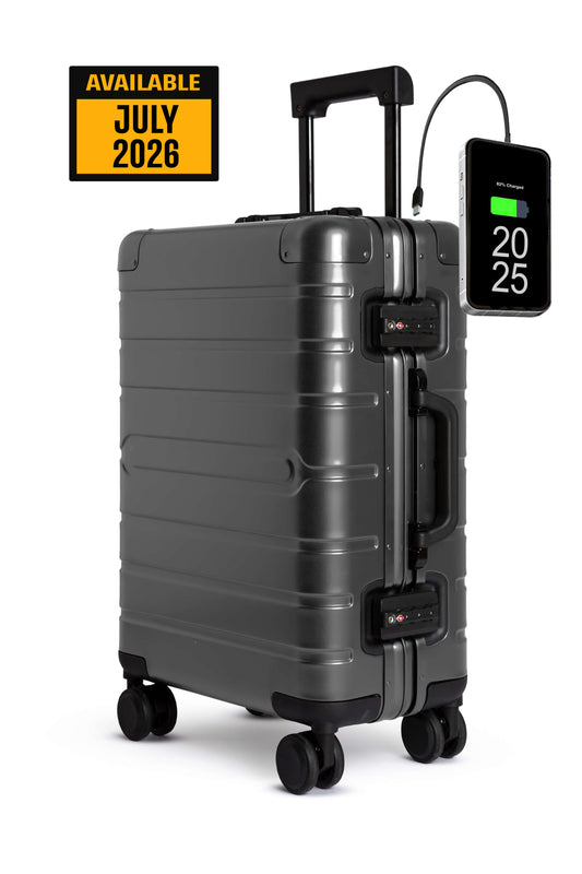 Valigia grigia in alluminio con display digitale ed etichetta "disponibile luglio 2026" su sfondo bianco