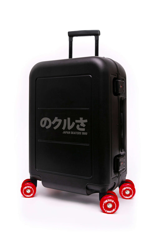 A matte black hard-shell spinner skate wheels suitcase with a telescoping handle extended, featuring the text 'のベンタ JAPAN SKATEBOYS 2016' in white on the front, and four bright red wheels with white lettering.