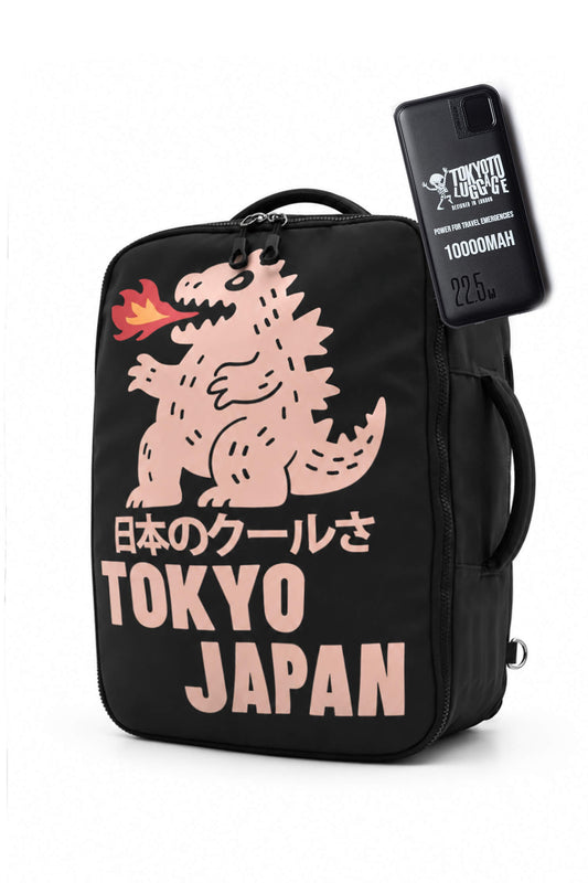 Una borsa termica nera per il pranzo con una grafica rosa di Godzilla, testo giapponese e la scritta «TOKYO JAPAN» in grandi lettere rosa. Una custodia nera per smartphone con il marchio «TOKYO GODZILLA 1000MAH» è mostrata fissata sul lato, su uno sfondo bianco.