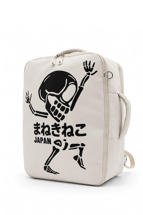 An off-white canvas backpack featuring a black graphic of a dancing skeleton with Japanese text and 'JAPAN' printed on the front, set against a plain white background.